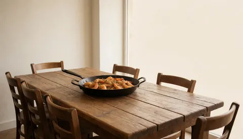 Cooked shrimp in a black skillet placed on a rustic wooden table in a restaurant with warm white walls and wooden chairs