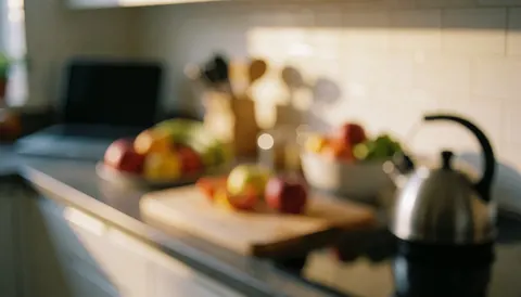 Fresh fruits, cutting board, and kettle on a kitchen counter illuminated by warm light, suitable for senior care backgrounds.
