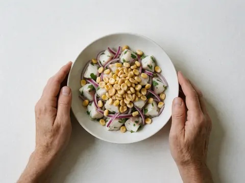 Fresh fish ceviche with toasted corn, red onion, and cilantro served on a white plate held by hands against a white background