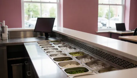 Ceviche bar counter displaying fresh ingredients on ice in stainless steel containers against pink walls with natural light