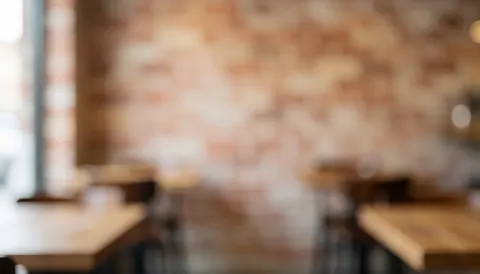Warm blurred pizzeria interior featuring a brick wall and wooden tables, serving as an ideal background for text overlays.