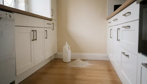 Bottle of diatomaceous earth powder on a clean kitchen floor near a beige wall, suitable for pest control services.