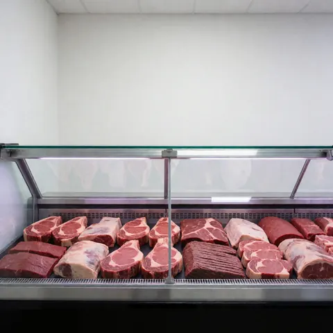 Fresh meat cut displayed in a refrigerated case with white walls and bright lighting, suitable for butcher shops.