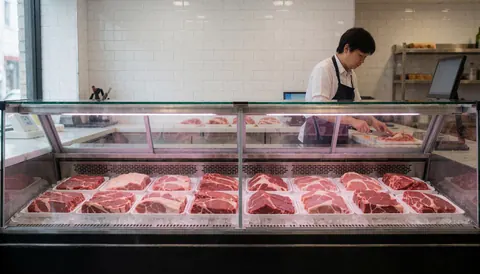 Fresh meat arranged in a glass display case inside a butcher shop with clean white tiles and professional lighting