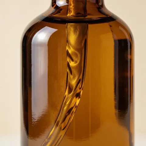 Amber glass bottle containing body oil with light reflections against a beige wall, showcasing a luxury beauty product.