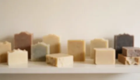 Artisan soaps arranged on a shelf in a perfumery with earth tones and warm white walls, suitable for a website background.