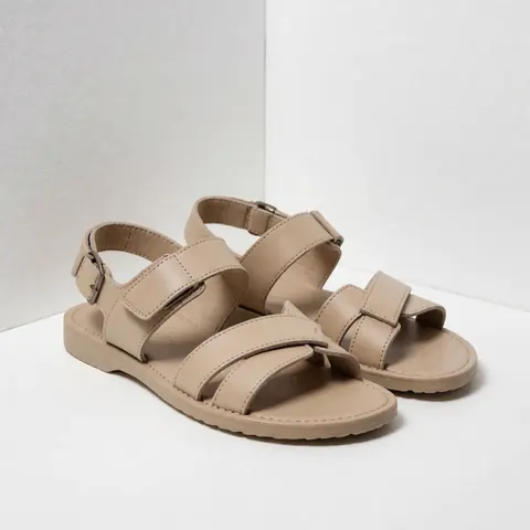 Beige leather sandals featuring crossed straps, flexible sole, and visible stitching on a white background