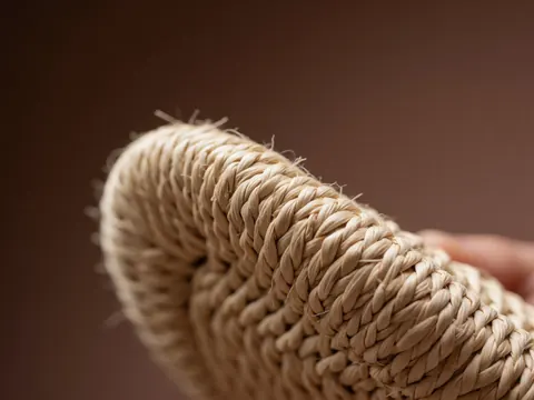 Macro detail of a woven sandal made with natural thread held in hand against a soft brown background