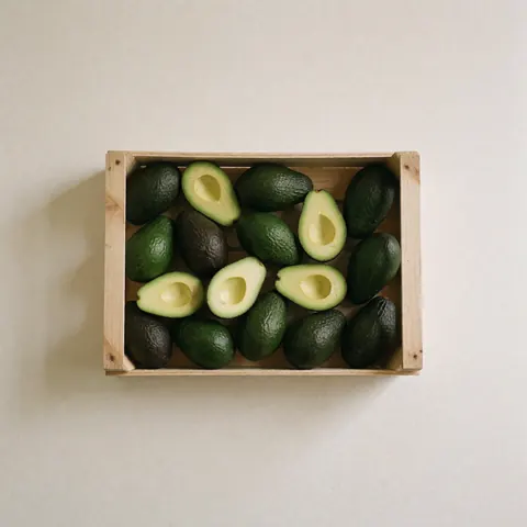 Whole and sliced green avocados arranged in a wooden crate on a white background for grocery store display