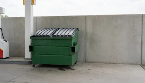 A green container placed next to a concrete wall at a gas station, suitable for commercial text backgrounds.
