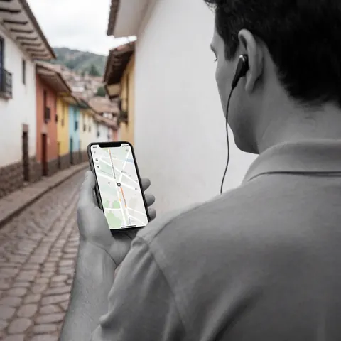 Tour guide walking on cobblestone street in San Blas, Cusco, using smartphone for navigation while wearing earpieces.