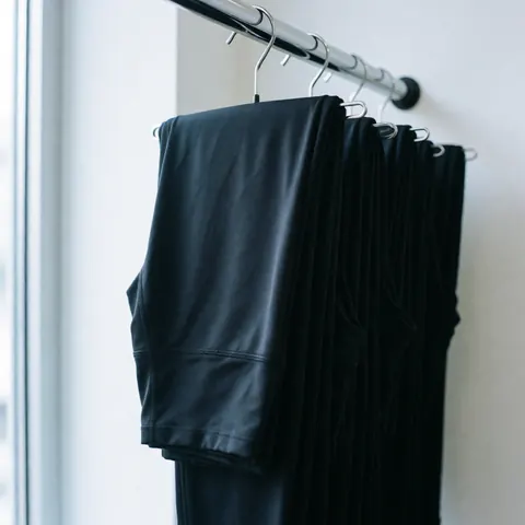 Folded black leggings hanging on a metal rack against a white wall with natural window light, ideal for sportswear product display.