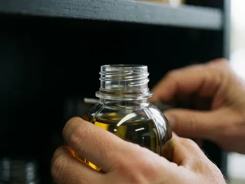 Close-up of hands holding a transparent plastic oil bottle with a cap, placed on a dark shelf, suitable for a gas station context.