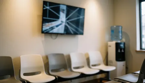 White waiting room chairs arranged near a wall-mounted television and water dispenser, suitable for professional service environments.