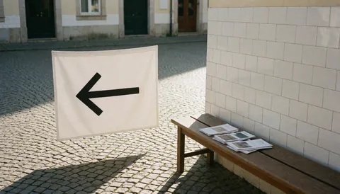 White flag with black left-pointing arrow on cobblestone plaza near wooden bench with brochures