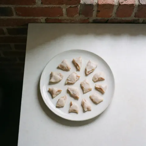 Neatly arranged pieces of clean offal on a white plate placed on a white counter with a red brick wall background and soft natural lighting.