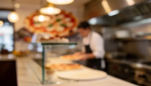 Soft focus background of a pizzeria kitchen featuring a chef, industrial stove, and pizza on the counter, ideal for text overlay