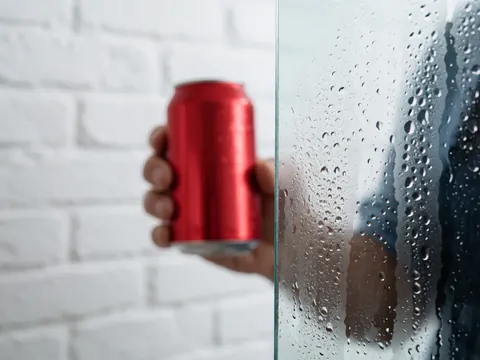 Close-up of condensation droplets on a refrigerator door with a cold can held in front, showcasing freshness and chill.