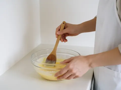 Hands in a white apron mixing yellow batter in a glass bowl on a white countertop at an ice cream shop